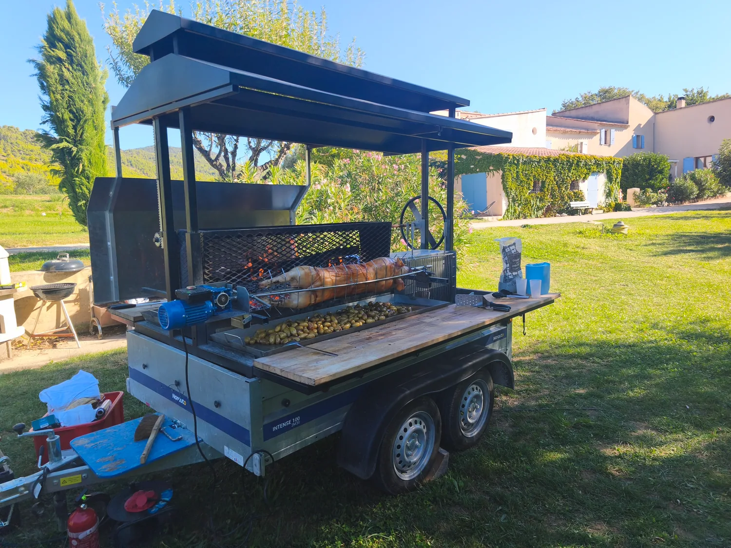 Le tournebroche mobile installé dans un jardin, cuisson en cours.